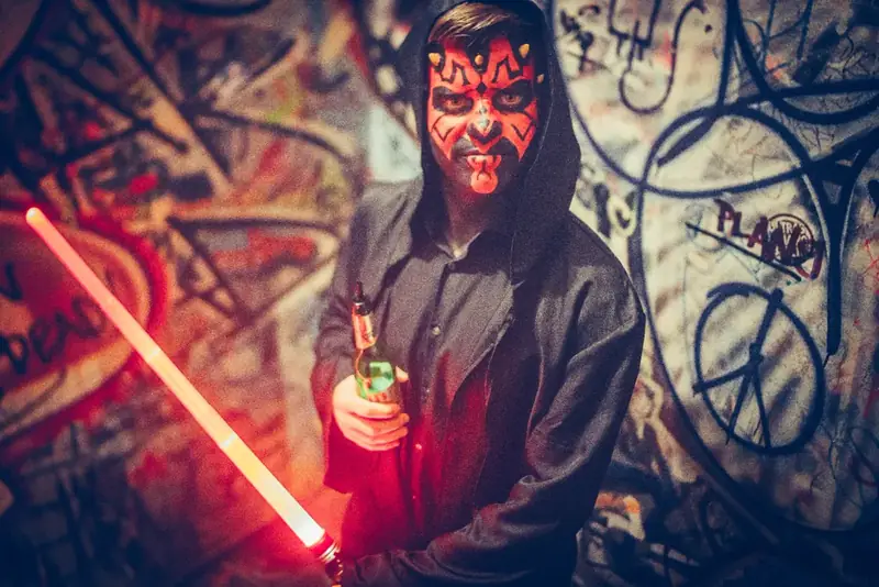 Maskierter Gast mit Lichtschwert vor Graffiti-Wand